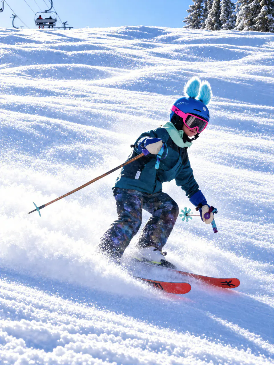 Young skier in a helmet with bunny ears carving down a sunny groomed run