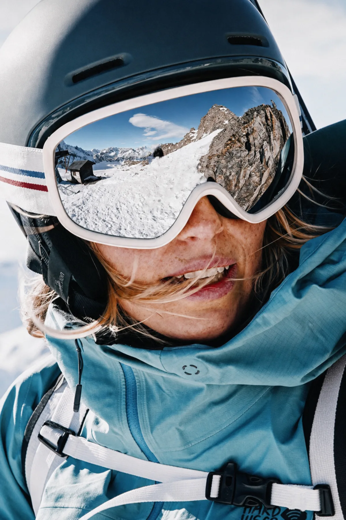 Skier in helmet and goggles with a snowy mountain reflected in the lenses
